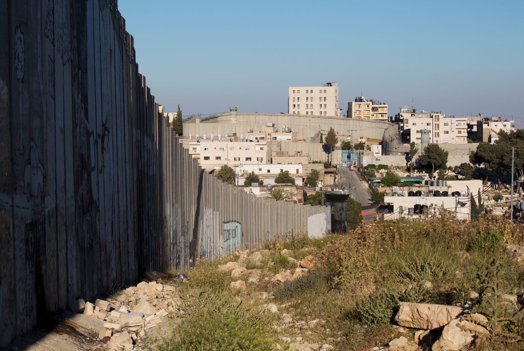 A high concrete wall runs through a valley, with houses next to the wall. A high concrete wall runs through a valley, with houses next to the wall.