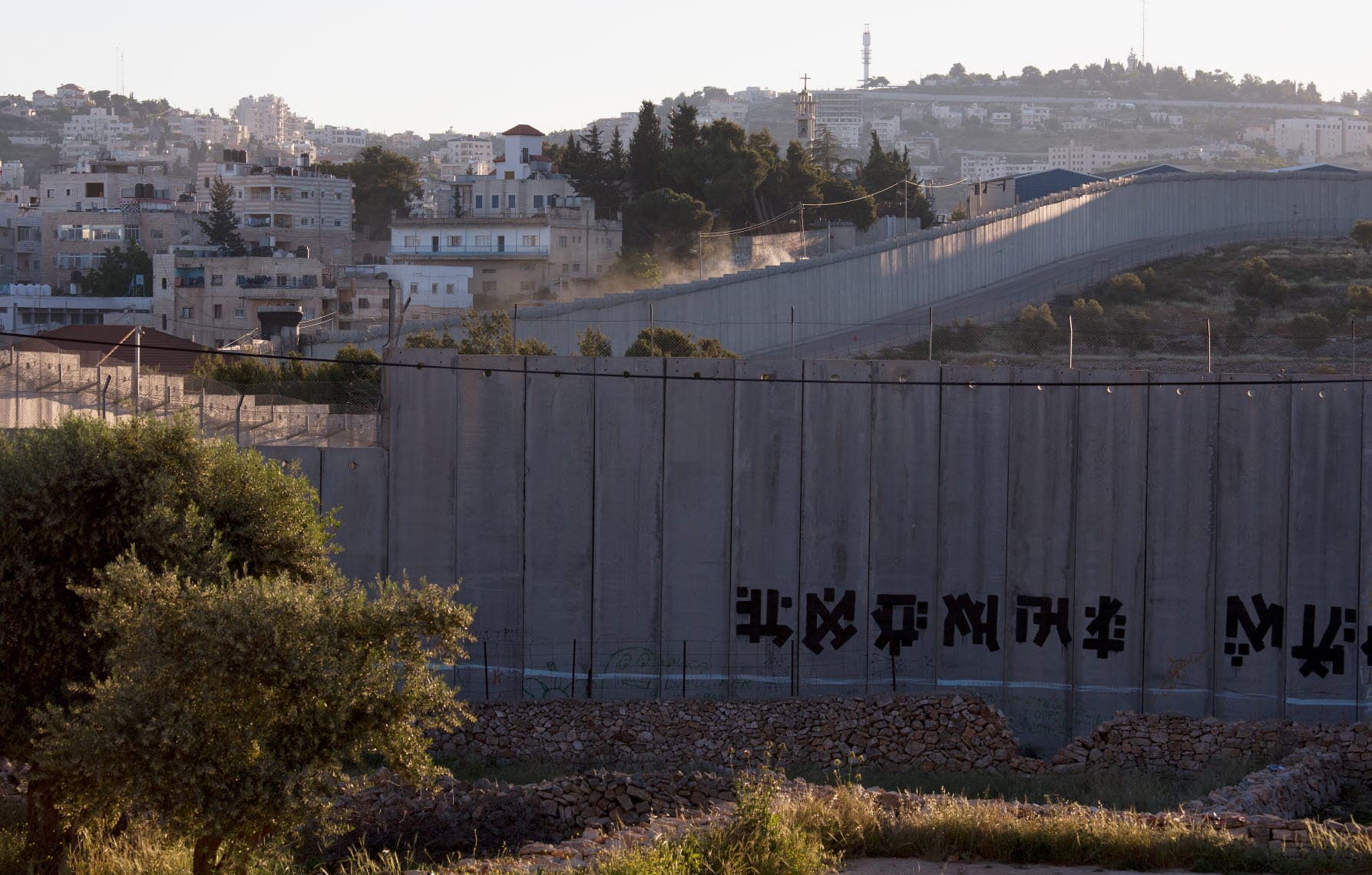 A high concrete wall runs over hills, with houses next to it. A high concrete wall runs over hills, with houses next to it.