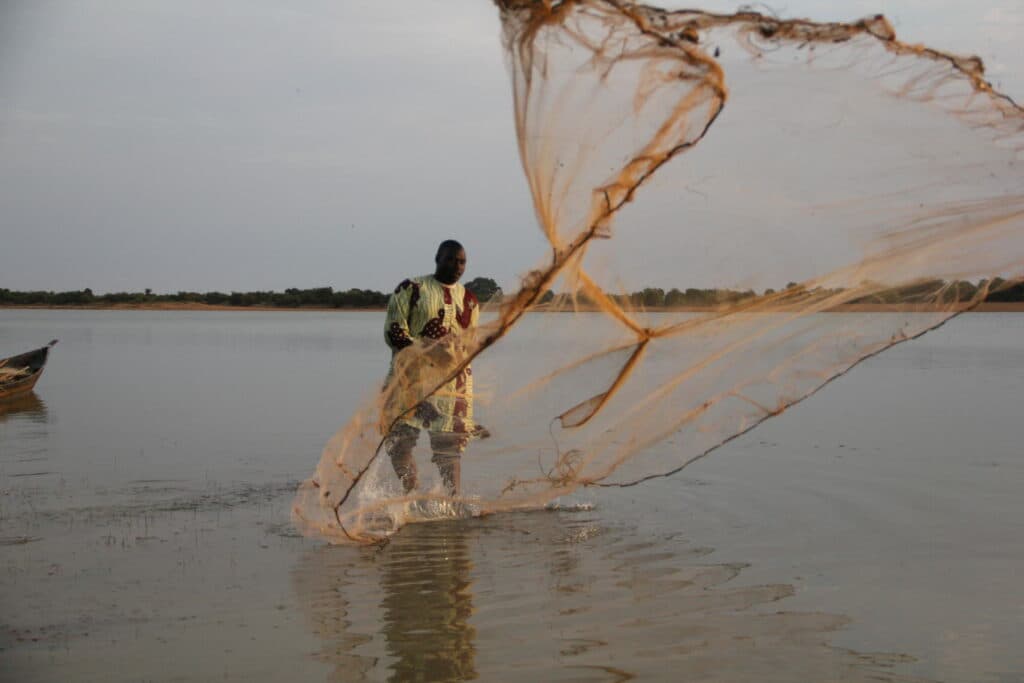 A person casting a fishining net in a lake. A person casting a fishining net in a lake.