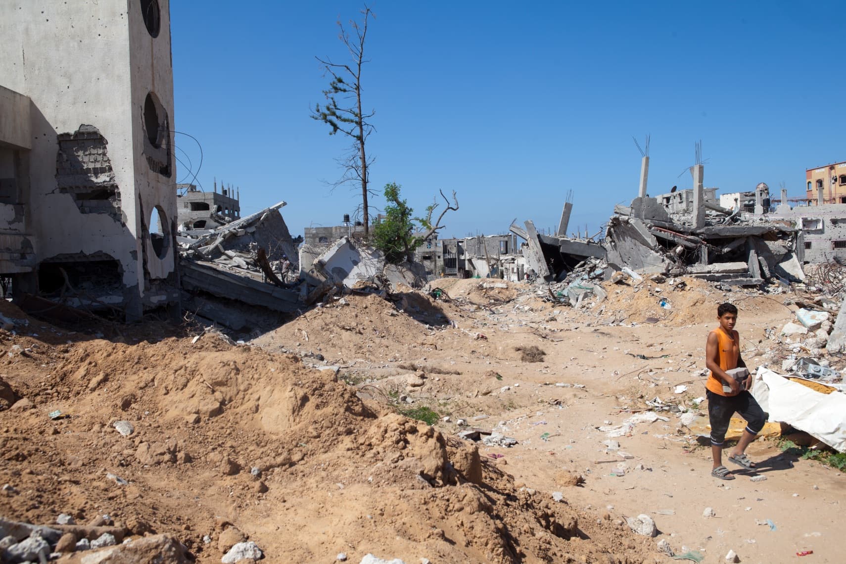 A person cleaning up rubble, with destroyed buildings in the background. A person cleaning up rubble, with destroyed buildings in the background.