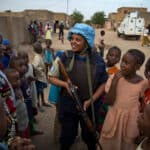 A female soldier with a blue helmet surrounded by women and girls.