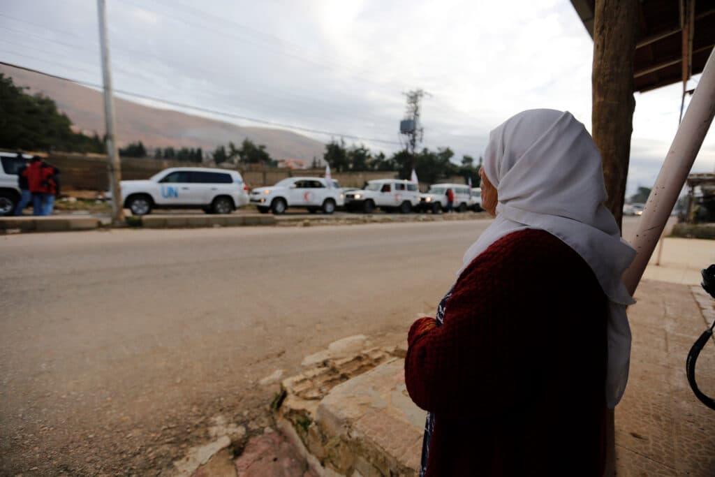 A woman watching United Nations vehicles, as part of a humanitarian convoy. A woman watching United Nations vehicles, as part of a humanitarian convoy.