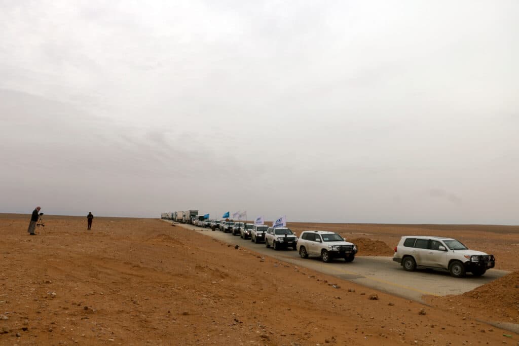 A convoy of cars with United Nations flags driving through dry land. A convoy of cars with United Nations flags driving through dry land.