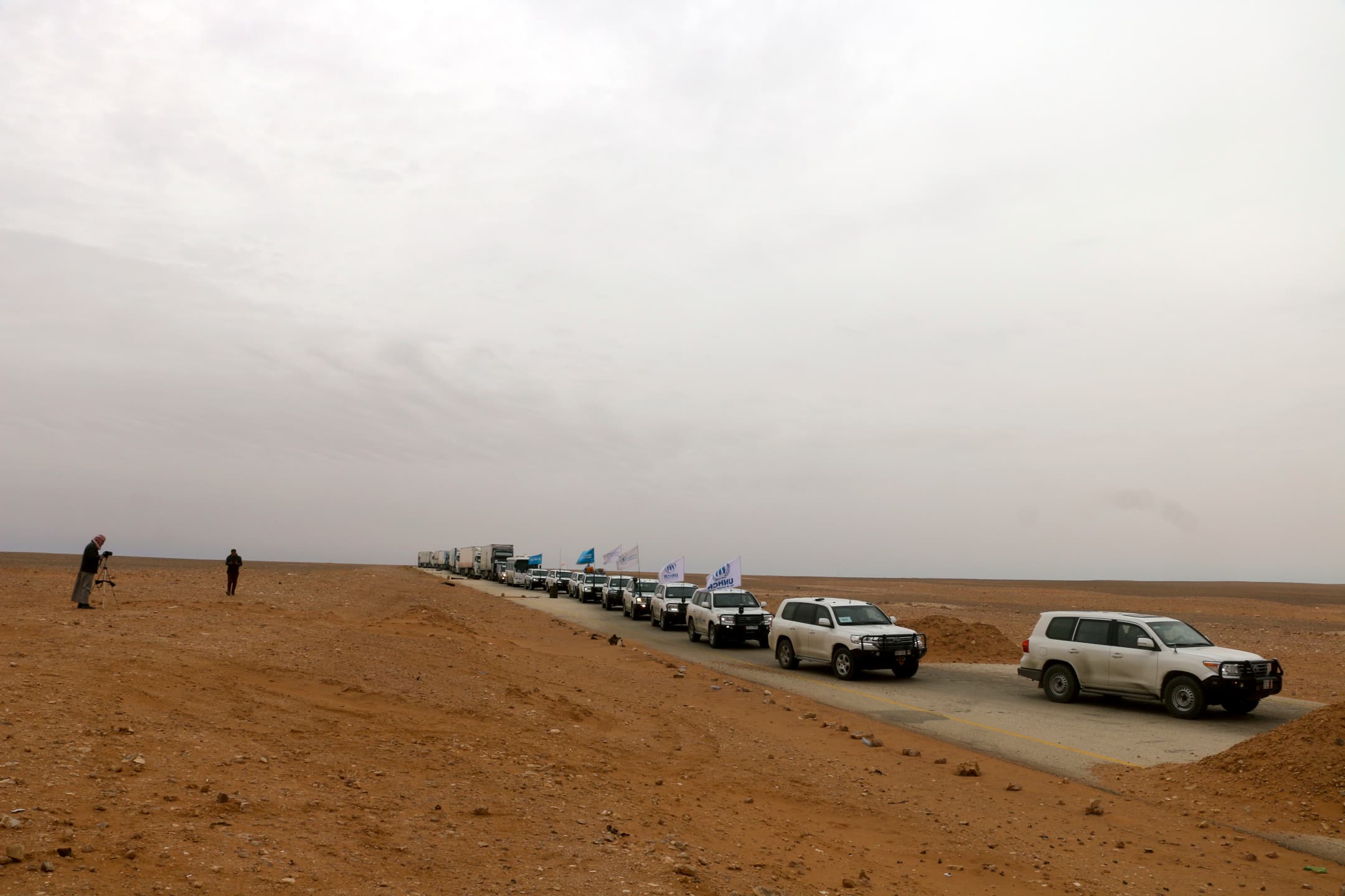 A convoy of cars with United Nations flags driving through dry land. A convoy of cars with United Nations flags driving through dry land.